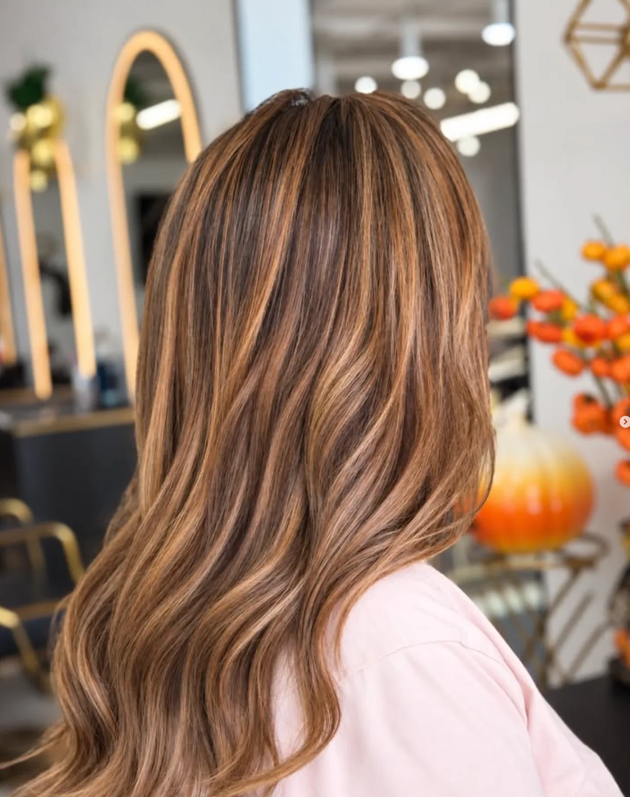 Brunette hair with caramel balayage and soft waves in the salon, in front of arched mirrors